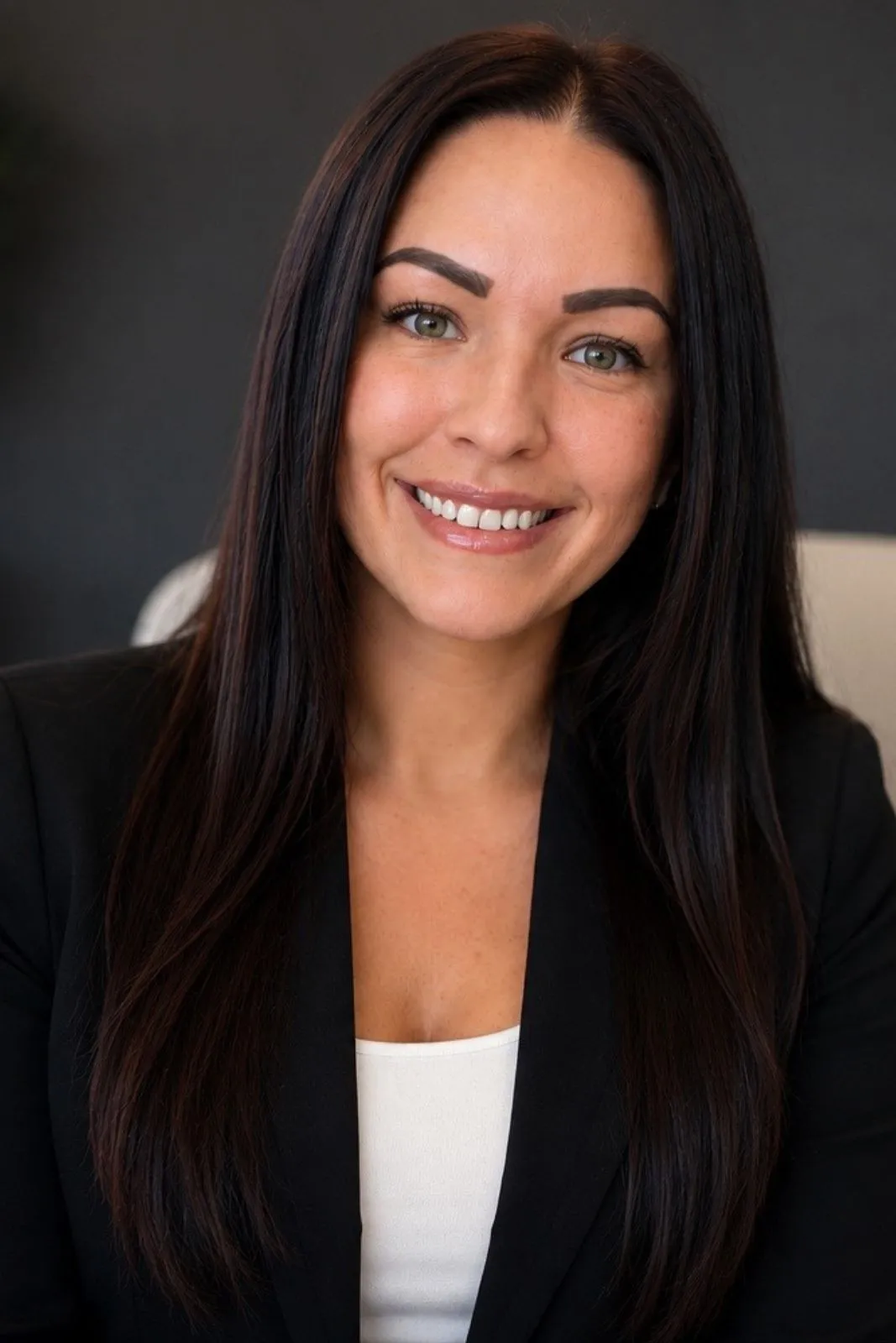 Professional headshot of a smiling woman with long dark hair, wearing a black blazer and white top.