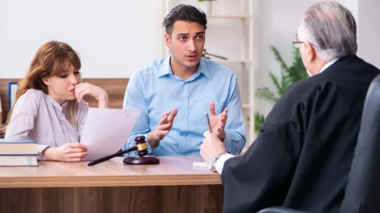 Three people in a legal consultation, with a judge listening to a young man and woman.