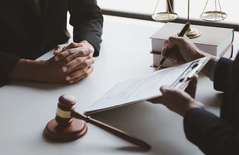 Two professionals in formal attire at a desk with legal books, a gavel, and a document being signed.