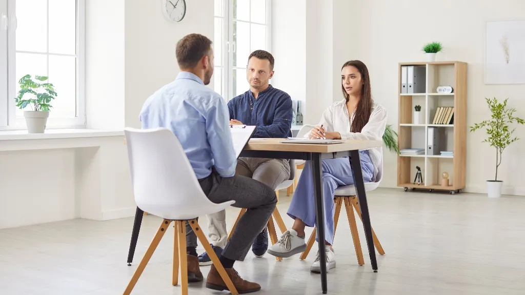 Three professionals engaged in a meeting around a wooden table in a bright office.