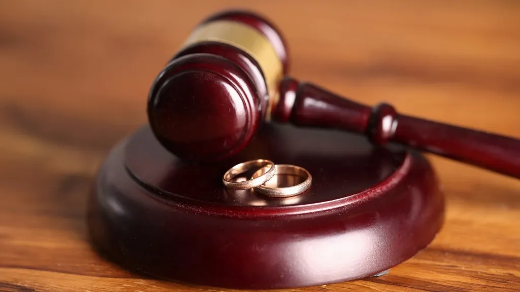 Close-up of a wooden judge's gavel resting on its base with two gold wedding rings.