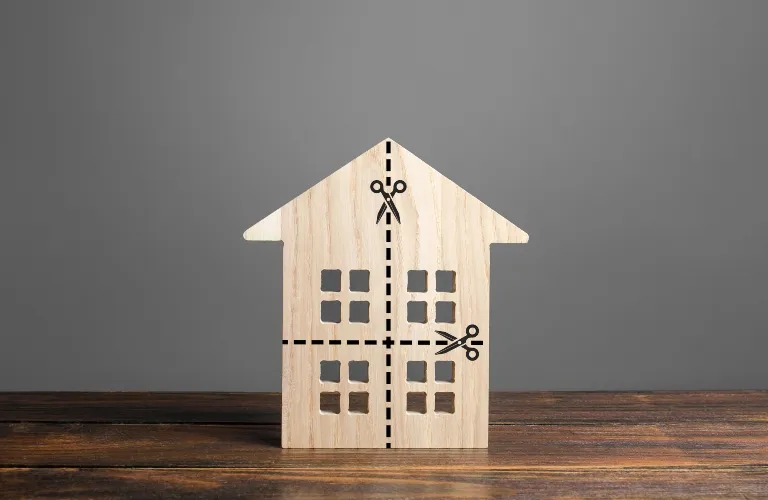 Wooden house model on wooden surface with black dashed lines and scissor icons.