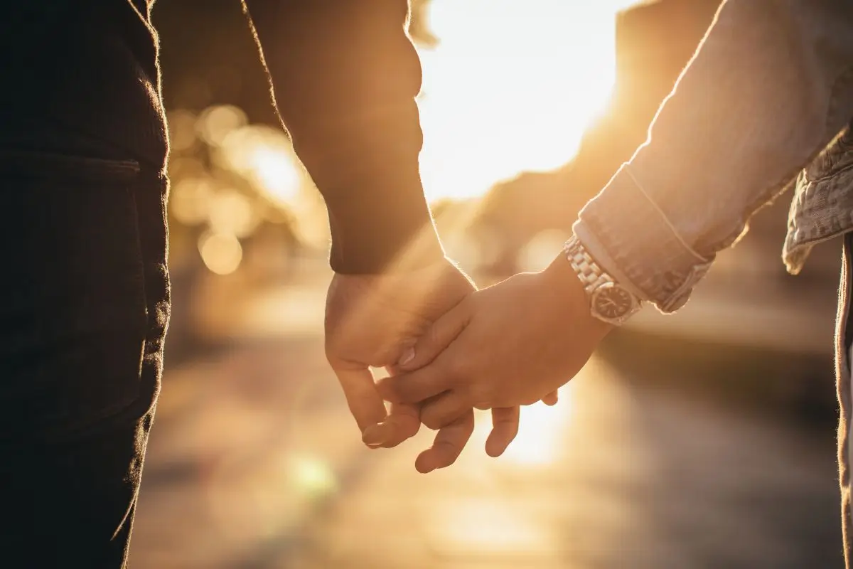Close-up of two people holding hands with sunlight in the background.