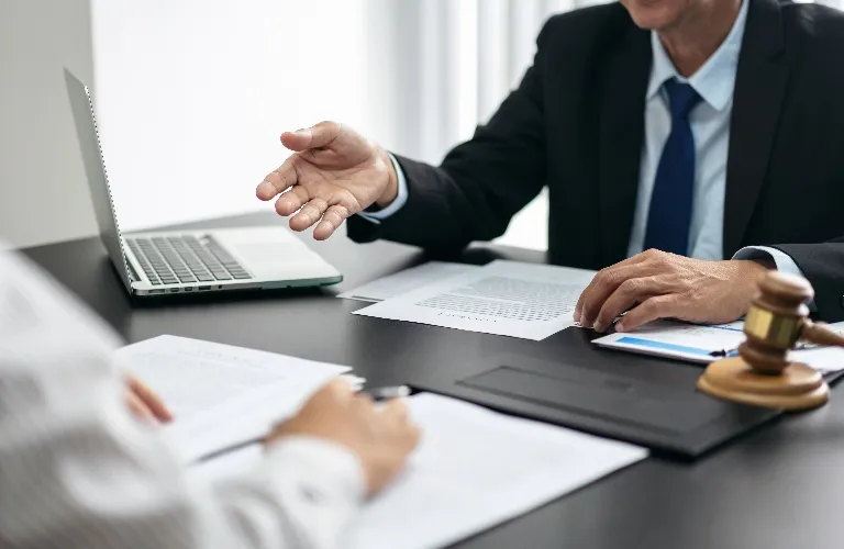 Two professionals in business attire discussing documents at a desk with a laptop and gavel.